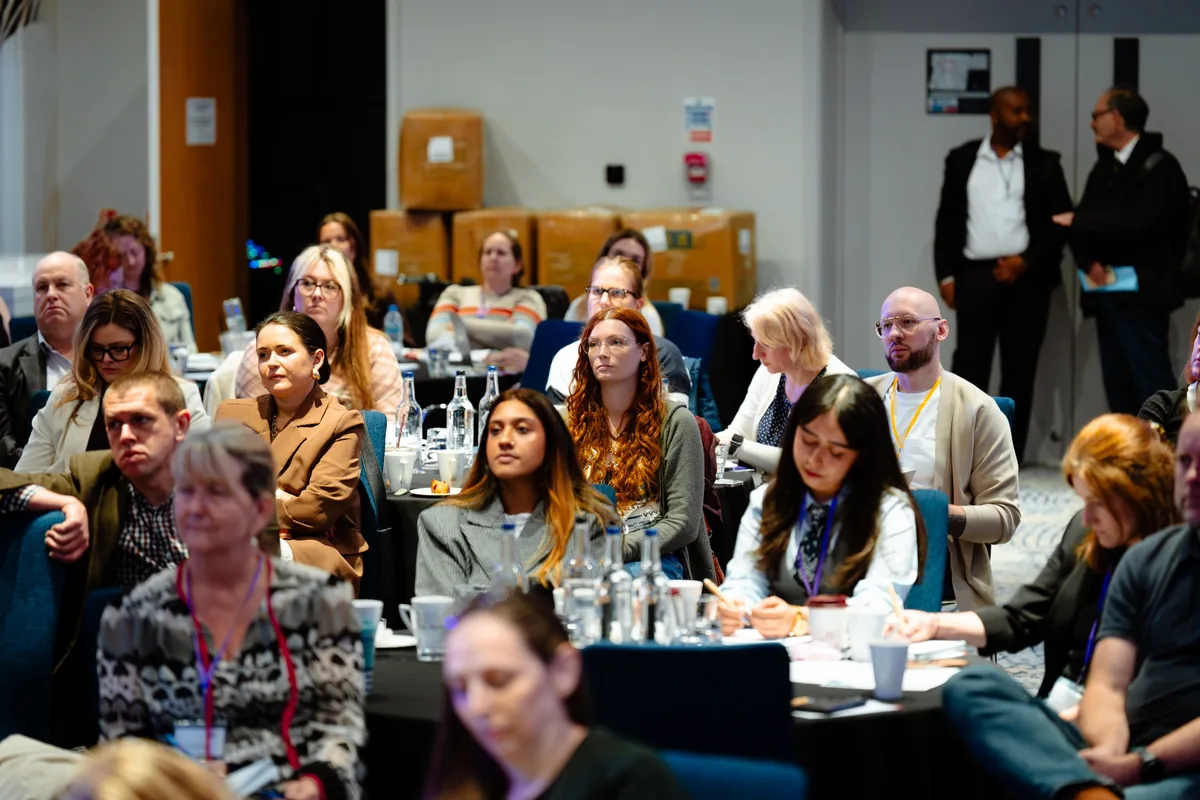 Audience members listening and taking notes at tables during a KBC event.