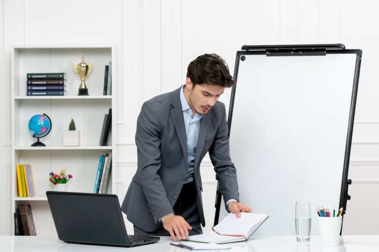 teacher-smart-instructor-grey-suit-classroom-with-computer-whiteboard-reading-notes